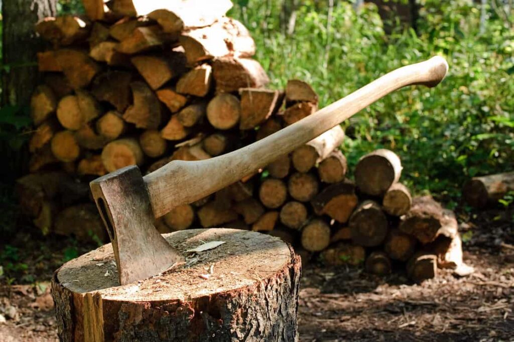 An axe stuck in a log in front of a pile of wood
