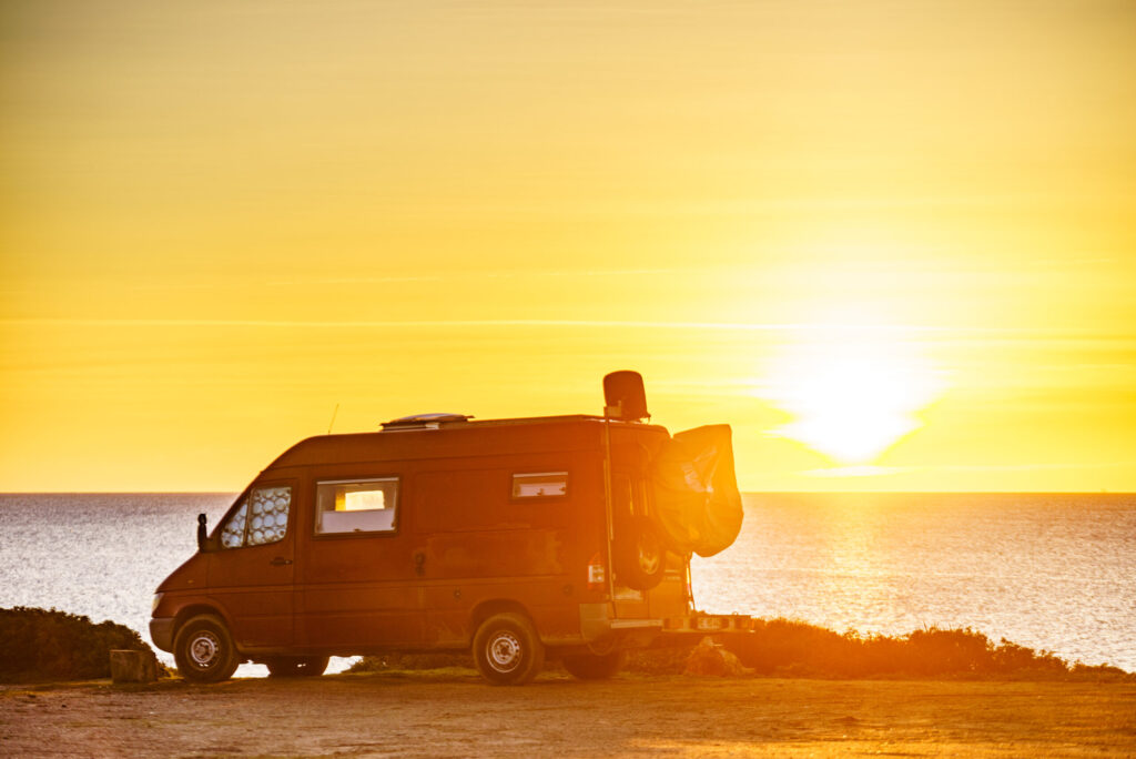 Camper van recreational vehicle at sunrise on mediterranean coast in Spain. Camping on nature beach. Vacation and traveling in motor home.