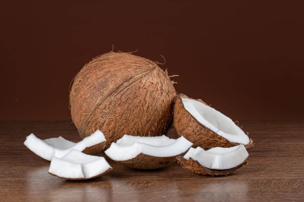 Coconut with half and pieces on brown background.
